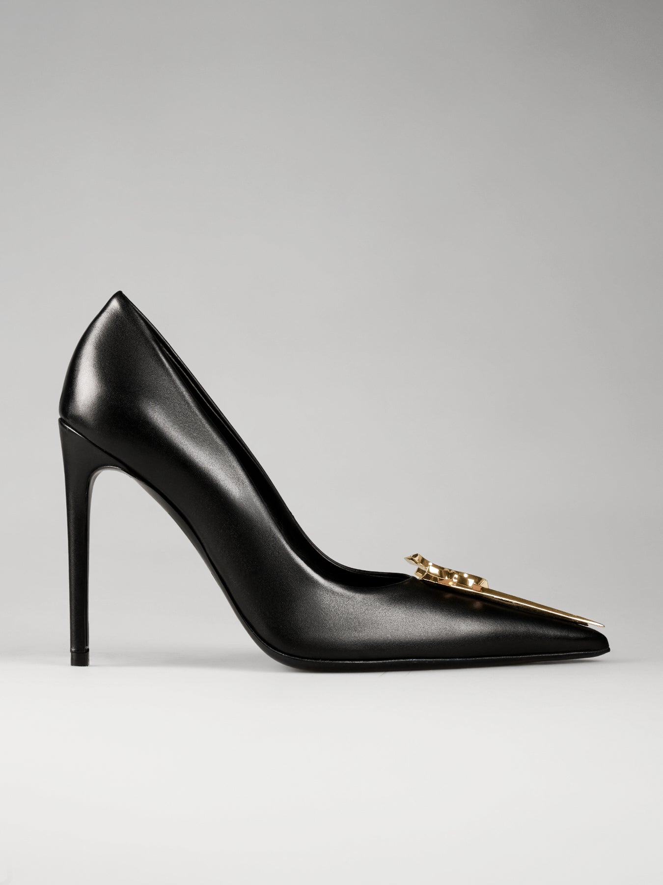 Black high-heeled shoe with a gold chain detail on a gray background
