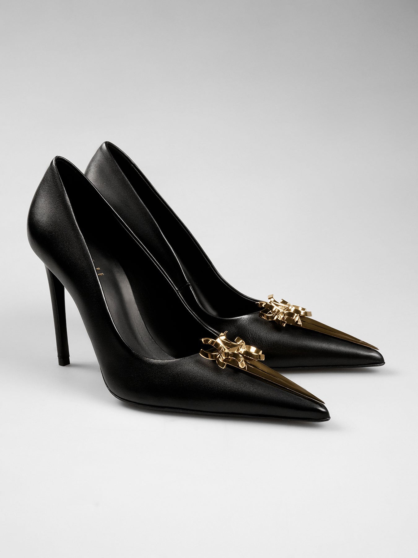 Black high-heeled shoes with gold accents on a light gray background